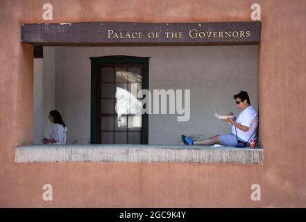 Eine Frau genießt das Mittagessen, während sie an einer Wand vor dem historischen Palast der Gouverneure aus dem 17. Jahrhundert in Santa Fe, New Mexico, sitzt. Stockfoto