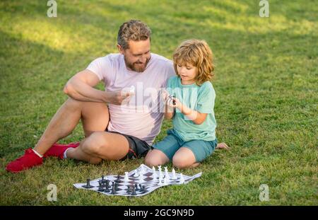 Nachhilfe. papa und Kind spielen Logik-Spiel. Vater und Sohn spielen Schach auf Gras im Park. Stockfoto