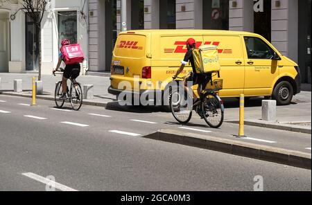 Bukarest, Rumänien - 02. August 2021 Panda und Glovo Lieferkuriere passieren einen gelben DHL Lieferwagen, der in der Nähe des Radweges auf der Calea Victori geparkt ist Stockfoto