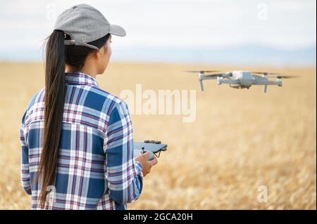 Weibliche Farmerin, die Drohne über Weizenfeld mit Steuerung fliegt, die Produktivität mit moderner Technologie überprüft. Hochwertige Fotos. Stockfoto