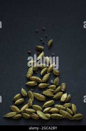 Vertikale kleine DOF Nahaufnahme von Cardamom Hülsen und Samen Haufen auf dem matt schwarzen Hintergrund. Es ist sehr beliebt in der indischen und Sri Lanka Küche. Stockfoto