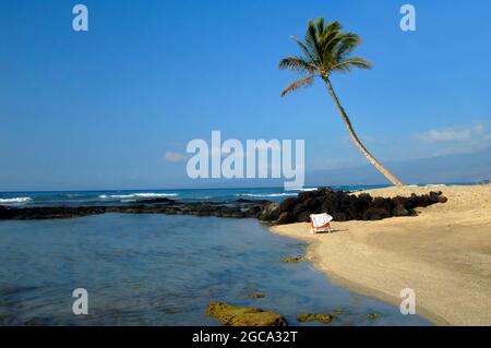 Der verlassene Strandstuhl liegt am Sand der Kohala-Küste auf der Big Island von Hawaii. Gelehnt Palme steht Wache über dieser ruhigen Strecke des sein Stockfoto