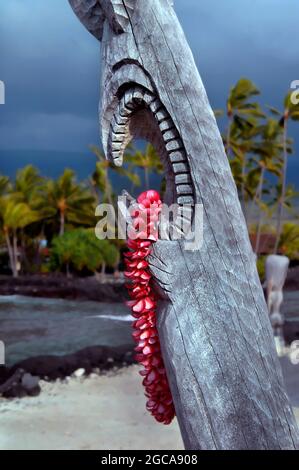 Wunderschöne rosa Plumeria lei hängt von der offenen Mündung eines hawaiianischen Tiki im Puuhonua o Honaunau National Historical Park auf der Big Island von Hawaii. Stockfoto