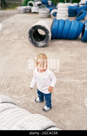 Lächelndes Kind, das auf einem Betonspielplatz neben einem Haufen bemalter Autoreifen steht Stockfoto