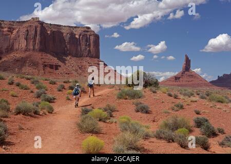 Zwei Personen wandern auf dem Wildcat Trail im Monument Valley Navajo Tribal Park, USA. Ein heißer augusttag mit blauem Himmel und Sandsteinfelsen, Buttes und Pinna Stockfoto