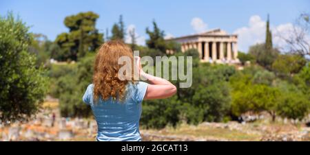 Mädchen Tourist macht Foto von Athen, Griechenland, Europa. Tempel des Hephaestus, Wahrzeichen von Athen in der Ferne. Junge hübsche Frau fotografiert Attraktionen o Stockfoto