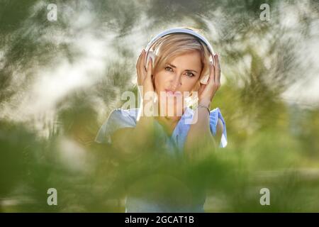 Blonde Frau in kabellosen Kopfhörern im öffentlichen Park. Stockfoto