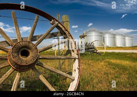 An einem Sommertag werden auf den Canadian Prairies ein altes Pferdewagenrad und Getreidesilos aufgestellt. Stockfoto