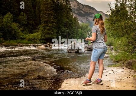 Ein junges Mädchen, das in Alberta, Kanada, einen Bergbach aus einem Felsen fischt. Stockfoto