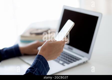 Hand des jungen Mannes, der mit Laptop-Computer und Smartphone-Mockup auf dem Schreibtisch zu Hause, Notebook und Telefon-Display leeren Bildschirm, Freiberufler Look Nachricht Stockfoto
