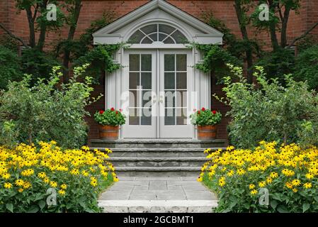 Eingangstür des Hauses, umgeben von leuchtend gelben Gänseblümchen Stockfoto