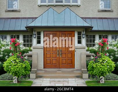 Elegante doppelte Holzmaserung Vordertür mit hellen Sommerblumen Stockfoto