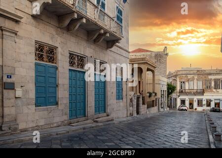 Syros, Kykladen, Griechenland. Farbenfroher Sonnenuntergang über traditionellen neoklassischen Gebäuden in der Hauptstadt Siros Hermoupolis. Leere Kopfsteinpflasterstraßen summieren sich Stockfoto