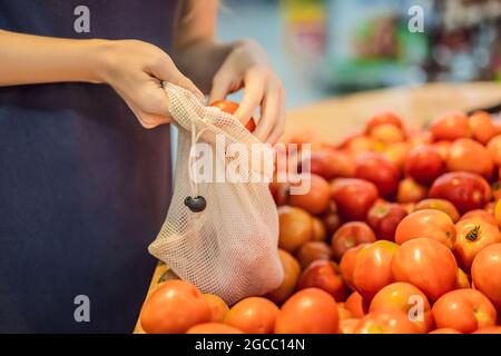 Eine Frau wählt Tomaten in einem Supermarkt ohne Plastikbeutel. Wiederverwendbare Tasche für den Kauf von Gemüse. Konzept ohne Verschwendung Stockfoto