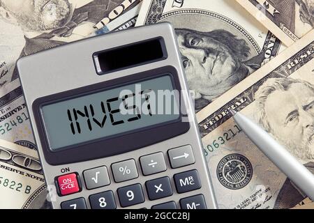 Das Wort Invest on Calculator Display mit Dollarschein Hintergrund. Finanzielle Investitions- und Ergebnisanalyse oder Berechnungskonzept. Stockfoto