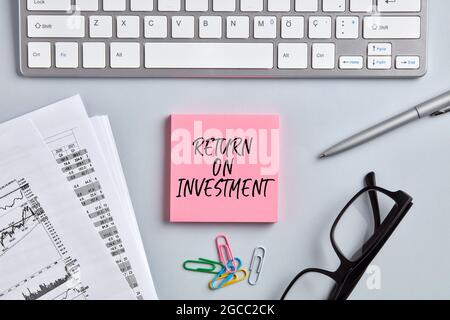 Das Wort Return on Investment auf pinkfarbenem Notizbuch für den Desktop-Arbeitsplatz im Büro. Business Finance-Konzept. Stockfoto