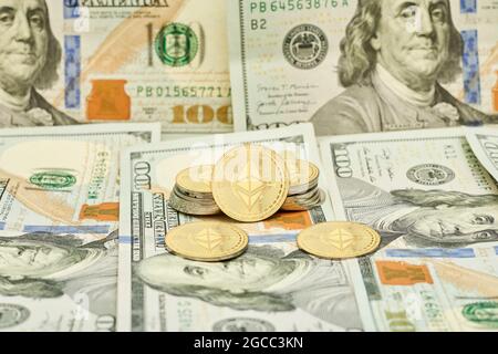 Goldene Krypto-Münzen und Haufen von US-Dollar. Ethereum-Münzen auf US-Dollar-Banknoten Stockfoto