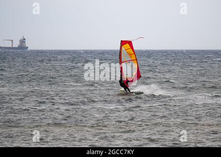 Oranges und rotes Windurf auf den Wellen in einem rauhen Meer. Stockfoto