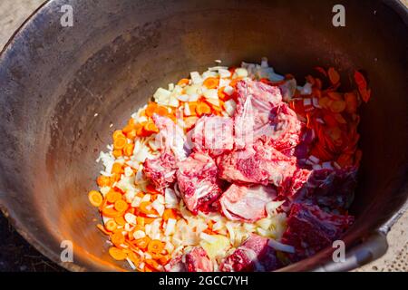 Oben Blick auf rohes Fleisch und frisches Gemüse, in einem alten Kessel gehackt, zubereitet zum Kochen von Gulascheintopf. Stockfoto