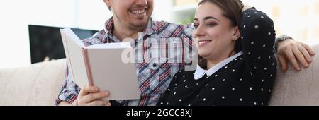 Lächelnder Mann und Frau sitzen auf der Couch und halten Buchen Stockfoto