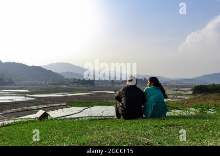 Das junge Paar, das am Abend auf einem Hügel mit Reisfeldern und Bergen im Hintergrund sitzt, wurde in ziro arunachal pradesh india aufgenommen. Stockfoto