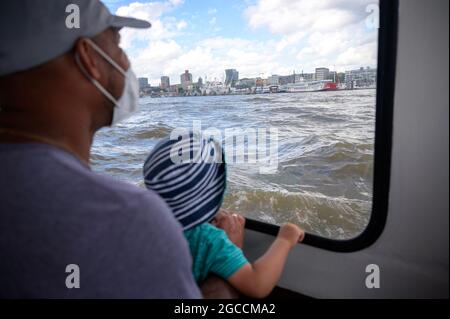 07. August 2021, Hamburg: Ein Mann trägt eine Nasenmaske und schaut mit seinem Sohn aus einem Hafenboot über die Elbe in Richtung Landungsbrücken. Foto: Jonas Walzberg/dpa Stockfoto