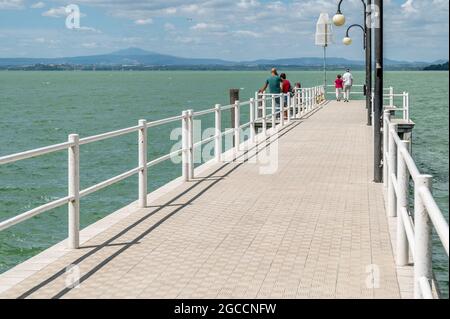 Einige schlendern auf der Seebrücke Passignano sul Trasimeno, Italien, die sich über den See erstreckt Stockfoto