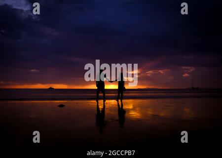 Silhouette des Paares halten sich die Hand und Happy Young Paar lieben am Strand bei Sonnenuntergang Stockfoto