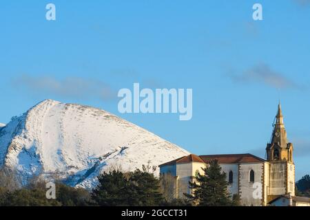 Die Kirche San Esteban de Galdames mit dem schneebedeckten Pico de la Cruz im Hintergrund Stockfoto