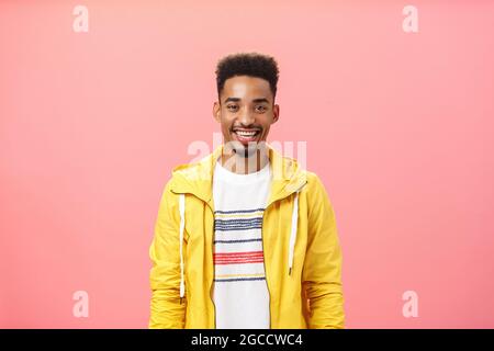 Waist-up-Aufnahme von charmanten freundlich gut aussehende dunkelhäutige Männchen mit Bart und Afro-Frisur in trendigen gelben Jacke lächeln mit zufrieden zufrieden zufrieden zufrieden Stockfoto