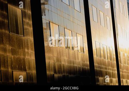 Die untergehende Sonne spiegelt sich in den Fenstern eines hohen Bürogebäudes aus Glas im alten Zentrum von Bukarest wider. Stockfoto