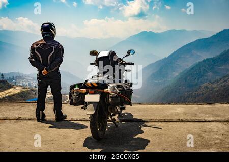 Ein Motorradfahrer, der das Tal von der Hügelspitze aus mit seinem beladenen Motorrad beobachtet, und das Bild mit der unberührten natürlichen Ansicht wurde bei der Bomdila arunachal pradesh india aufgenommen. Stockfoto