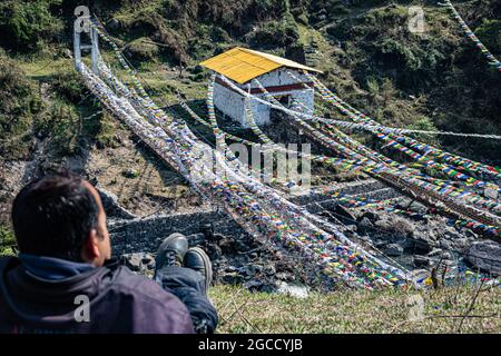 Der Mann, der die alte heilige Eisenbrücke mit vielen buddhistischen heiligen Fahnen aus dem oberen Winkel beobachtet, wird an der Chaksambrücke tawang arunachal pradesh india aufgenommen. Stockfoto