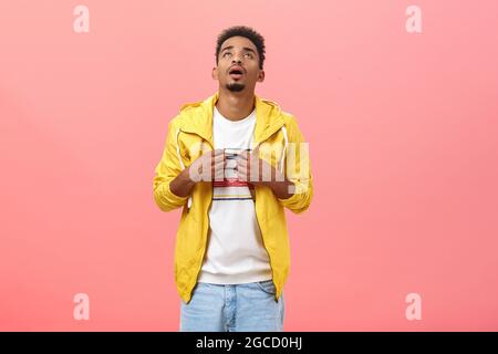 Stilvoller dunkelhäutiger Mann, der unter heißem Wetter leidet und mit einem T-Shirt winkt, um sich in Unannehmlichkeiten auf einem rosa Hintergrund zu kühlen Stockfoto