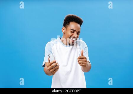 Schöne Dinge, die mich glücklicher machen. Porträt eines charmanten enthusiastischen afroamerikanischen Mannes mit Bart, der fröhlich tanzt und mit dem Smartphone mitsingt Stockfoto