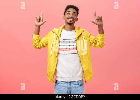 Studio-Aufnahme eines glücklichen enthusiastischen, gutaussehenden dunkelhäutigen männlichen Studenten mit Bart und lockiger Frisur, die mit zufriedener Freude aussahen und nach oben zeigen Stockfoto