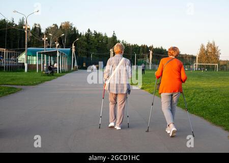 Nordic Walking mit Stöcken. Rentner kümmern sich um ihre Gesundheit. Abendlicher Spaziergang entlang der Straße. Großmütter trainieren Muskeln. Frauen gehen in der Stockfoto