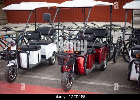 Moto-Elektrofahrzeuge sind in einer Reihe. Verleih von Elektrofahrrädern. Scheinwerfer an Fahrzeugen mit zwei Rädern. Motorradverkauf. Massenparkplätze für Fahrzeuge. Modern urban Stockfoto