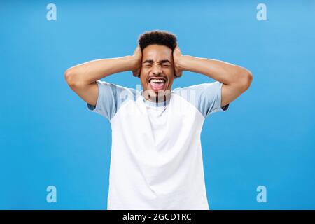 Überwältigend aus vielen Informationen. Porträt eines verzweifelten afroamerikanischen Studenten im T-Shirt, der die Hände am Kopf hält und mit dem er brüllt Stockfoto