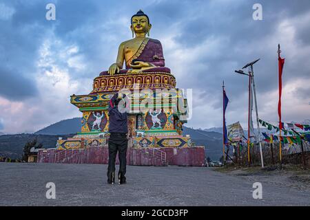 Mann, der am Abend an einer isolierten riesigen goldenen Buddha-Statue mit launigem Himmel betet Stockfoto