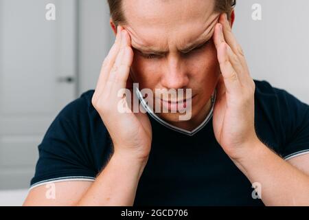 Kaukasischer Mann, der zu Hause sitzt und unter Kopfschmerzen leidet. Stockfoto