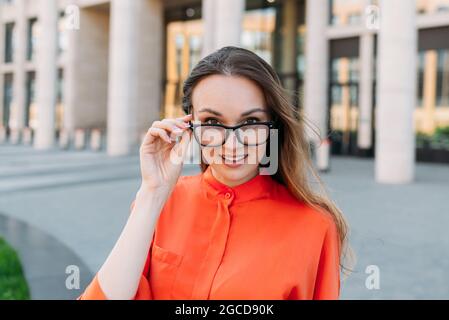 Junge kaukasische Frau mit Brille in der Stadt lächelt vor der Kamera. Stockfoto