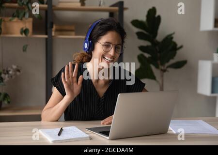 Nahaufnahme lächelnde Frau in Kopfhörern, die Hand an die Webcam schwenkt Stockfoto