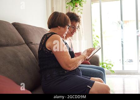 Ältere Frau und Tochter teilen sich das Tablet, während sie Familienfotos ansehen Stockfoto