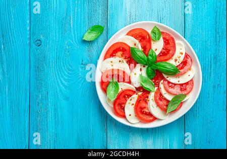 Caprese-Salat mit frischen Tomaten, Mozzarella-Käse und Basilikumblättern auf blauem Hintergrund. Stockfoto