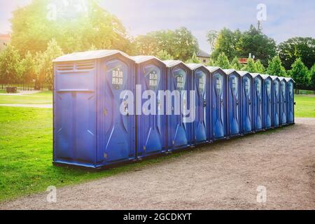 Reihe von zwölf blauen Bajamaja-tragbaren Toiletten im Park für einen Veranstaltungsort im Freien. Helsinki, Finnland. 7. August 2021. Stockfoto