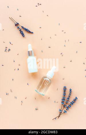 Lavendel natürliches kosmetisches Serum und ätherisches Öl auf pastellorangenen Hintergrund mit Blumen. Aromatherapie, Hautpflege Kosmetik Konzept. Draufsicht, flach l Stockfoto