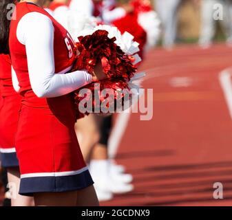 High School Cheerleader stehen auf einer roten Spur und halten ihre Pom Poms vor sich. Stockfoto