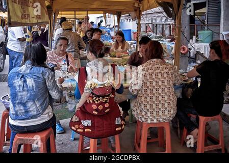 Mutter mit Baby in einem Rückenschlingengeschirr getragen und in einem Freiluftrestaurant gegessen. Thailand S. E. Asien Stockfoto