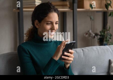 Nahaufnahme einer glücklichen jungen Frau mit dem Smartphone, die sich auf der Couch entspannt Stockfoto